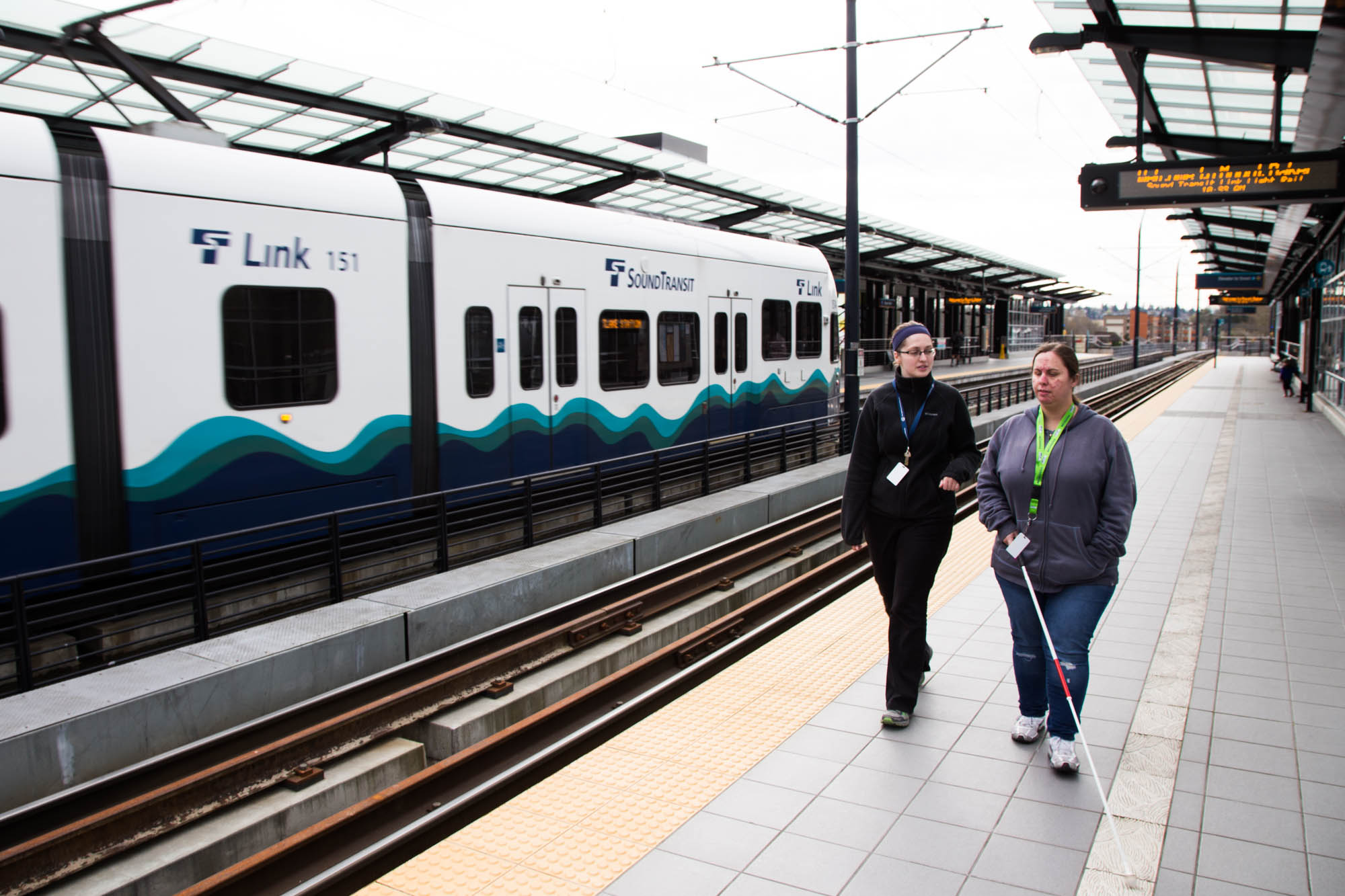 OandM-1 Orientation and Mobility instructor Erin Fitzpatrick (left) works with training a Lighthouse employee at the Mount Baker Light Rail station in Seattle, WA