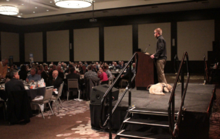 Keynote speaker Jake Olson (right) speaks to the audience at the Luncheon