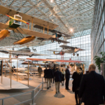Guests walking through the Museum of Flight underneath vintage airplanes hanging above