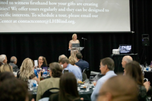 woman speaking with people seated at tables