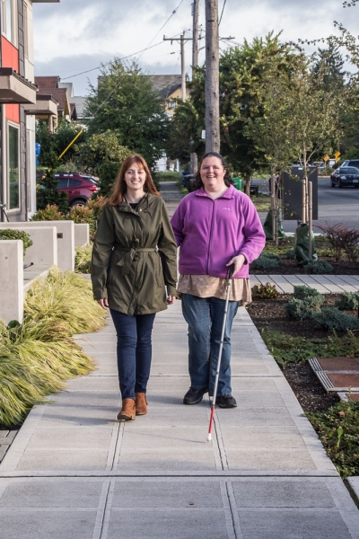 Erin and student walking with cane in neighborhood street and smiling