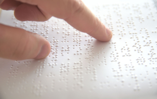 A close up photo of a hand reading a braille page, shown from the side.