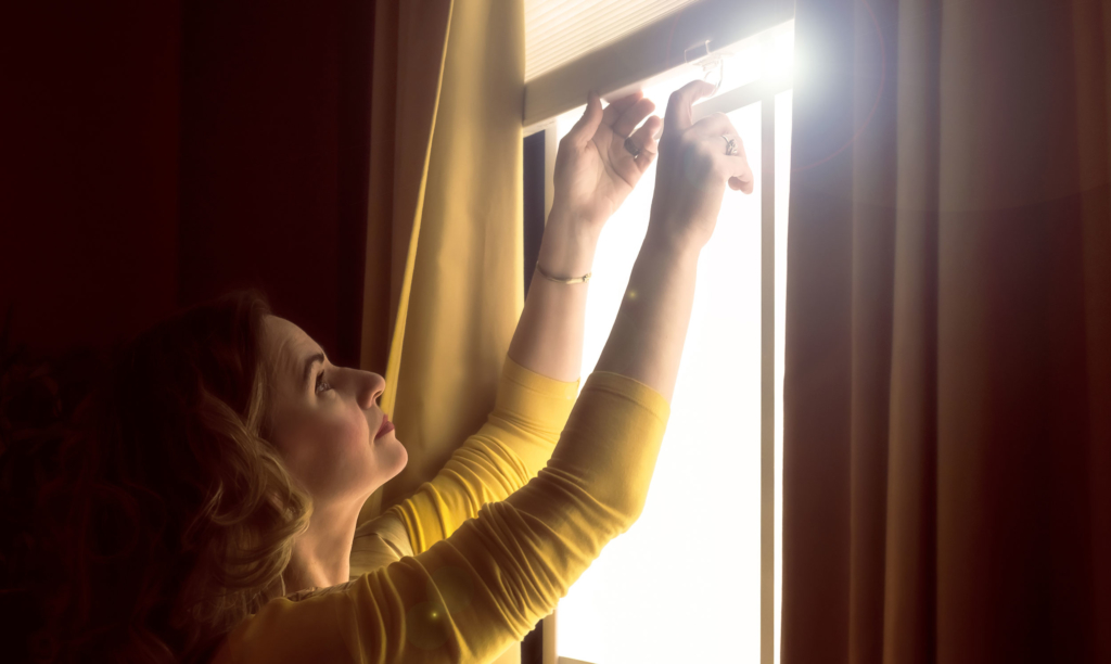 An image of a woman pulling down window blinds. 