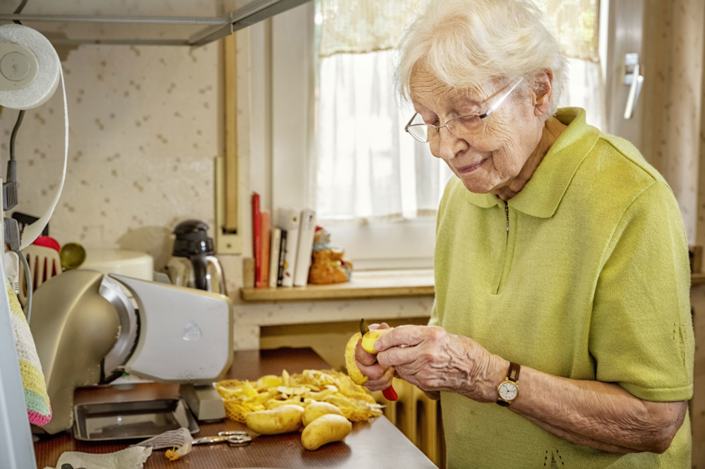 Older white woman standing at kitchen counter, peeling potatoes