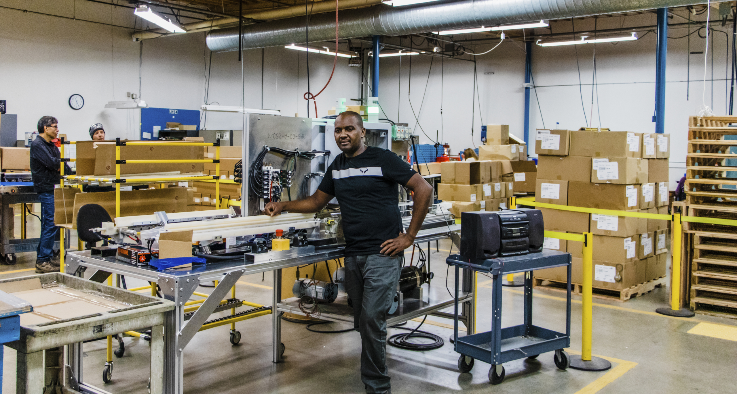 John Koigi stands in a machine shop next to a machine.