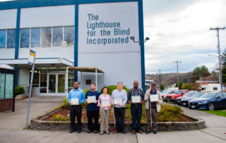 Photo of six people standing outside a building reading, "The Lighthouse for the Blind, Inc."