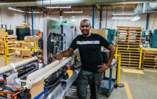 A dark skinned man standing proudly in front a machining workstation in Seattle