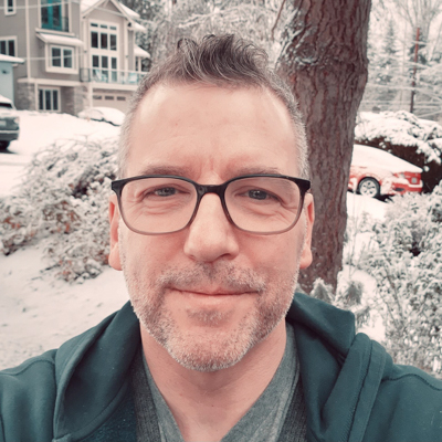 Selfie of Kirk, a light skinned man with glasses and a goatee, smiling in a snowy driveway