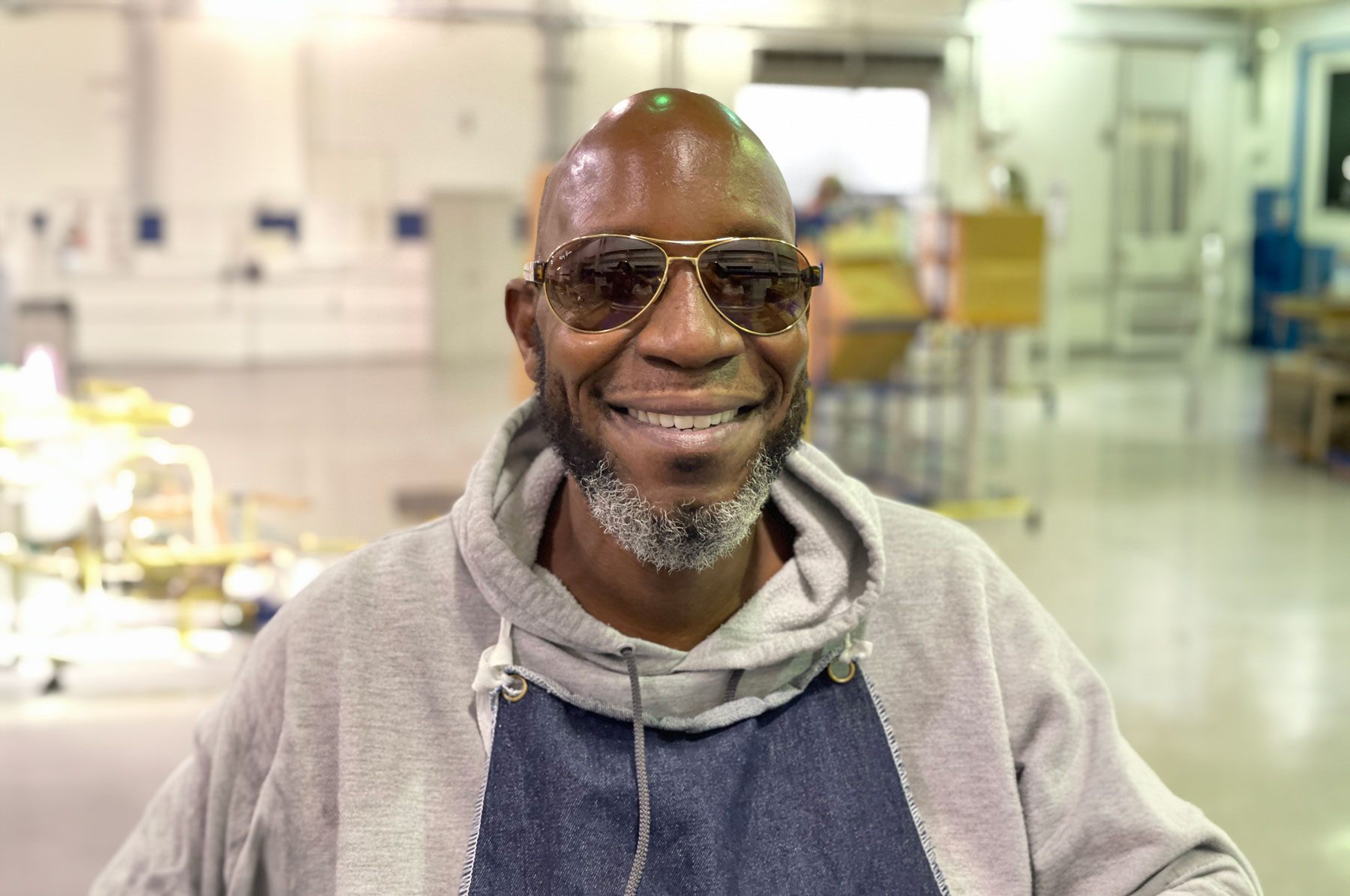 A portrait of a dark skinned man with a bald head smiling and wearing sunglasses.