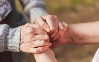 Close up image of two hands grasping two older, more wrinkled hands.
