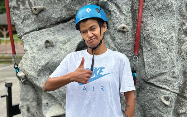 Rose Rosas, DeafBlind retreat camper. Rose has medium dark skin and is holding a thumbs up while wearing a rock climbing helmet.