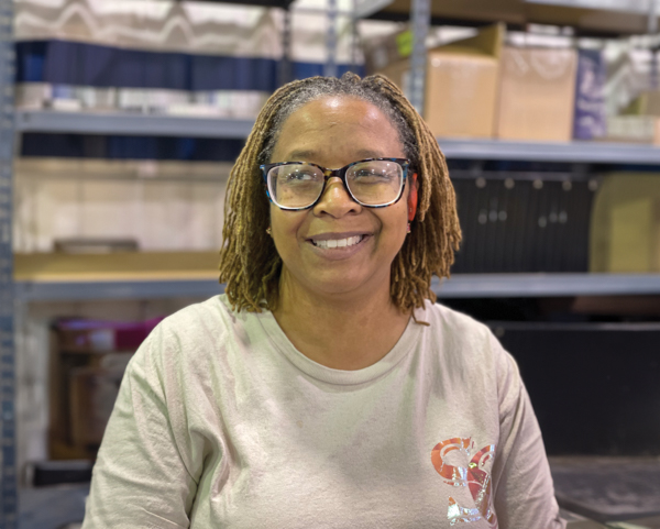 Pendah Goode, Production Worker, Summerville Facility. Pendah has medium dark skin, and shoulder length blonde and brown braids. She is wearing glasses and smiling.