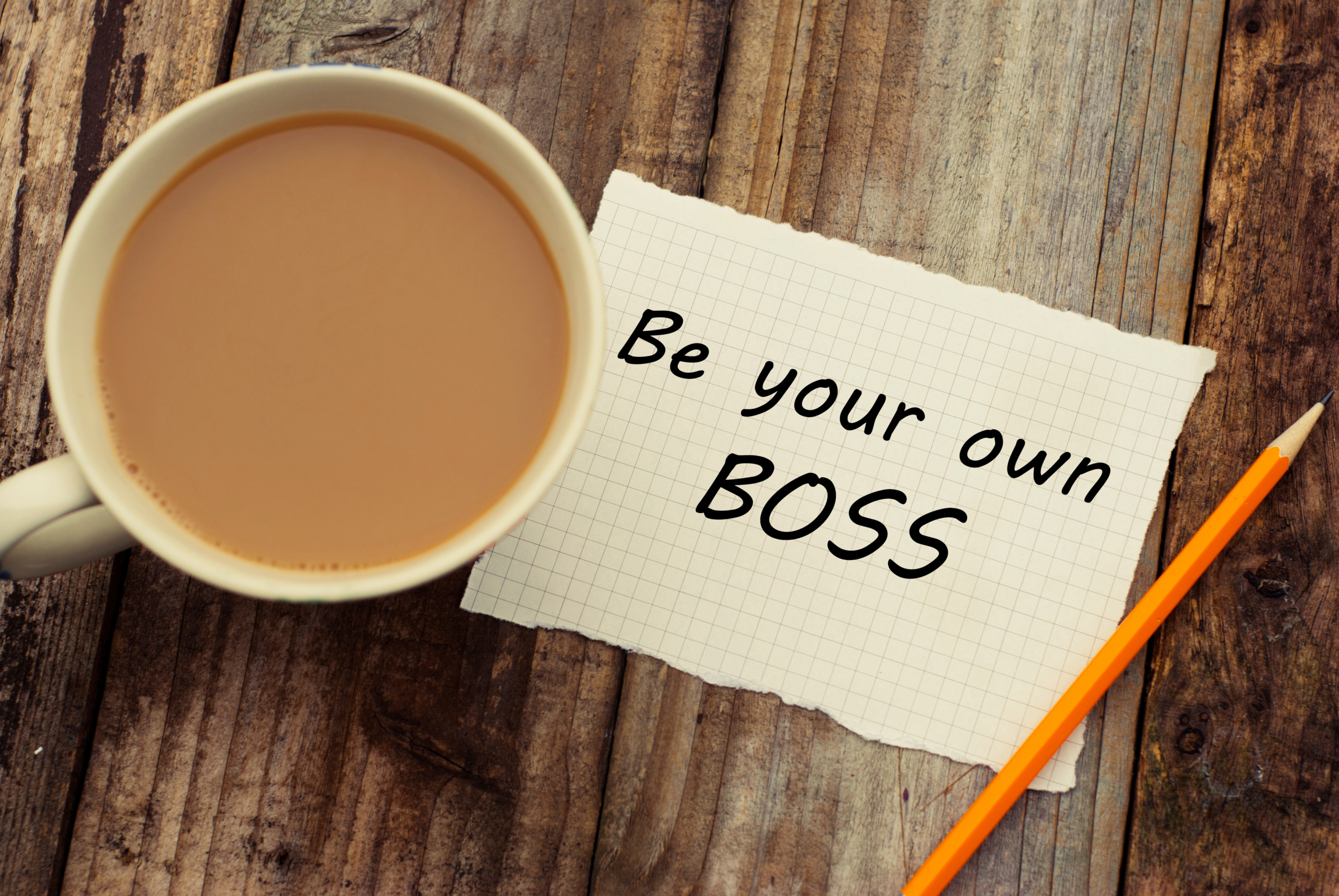 Image of a cup of coffee on a table, with a piece of paper that states "Be your own boss."