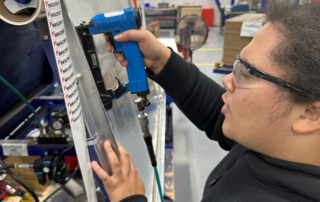 Woman uses a nail gun to assemble a wallboard.