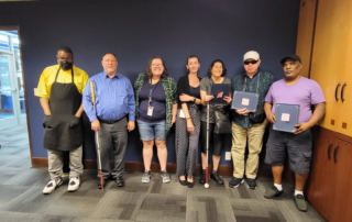 Group of 6 employees stand along a wall, smiling with then CEO George Abbott.