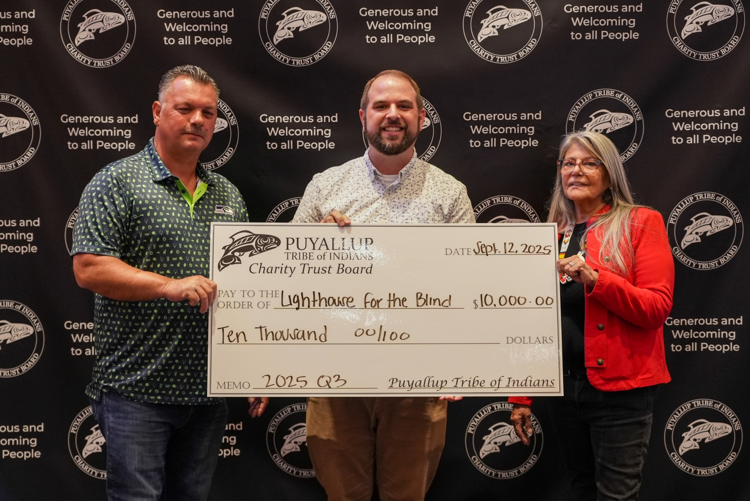 Two men and one woman hold an oversized check in the amount of $10,000