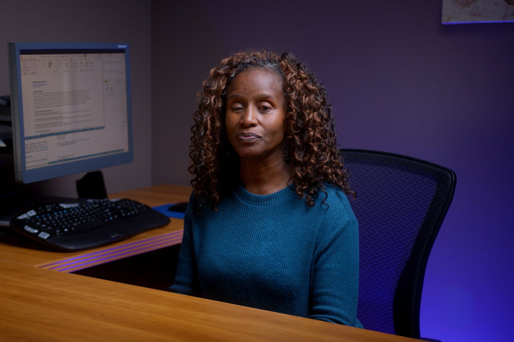 Cathy-Wilson-HR-Generalist Photo of Cathy, a dark-skinned woman sitting at her computer workstation and smiling
