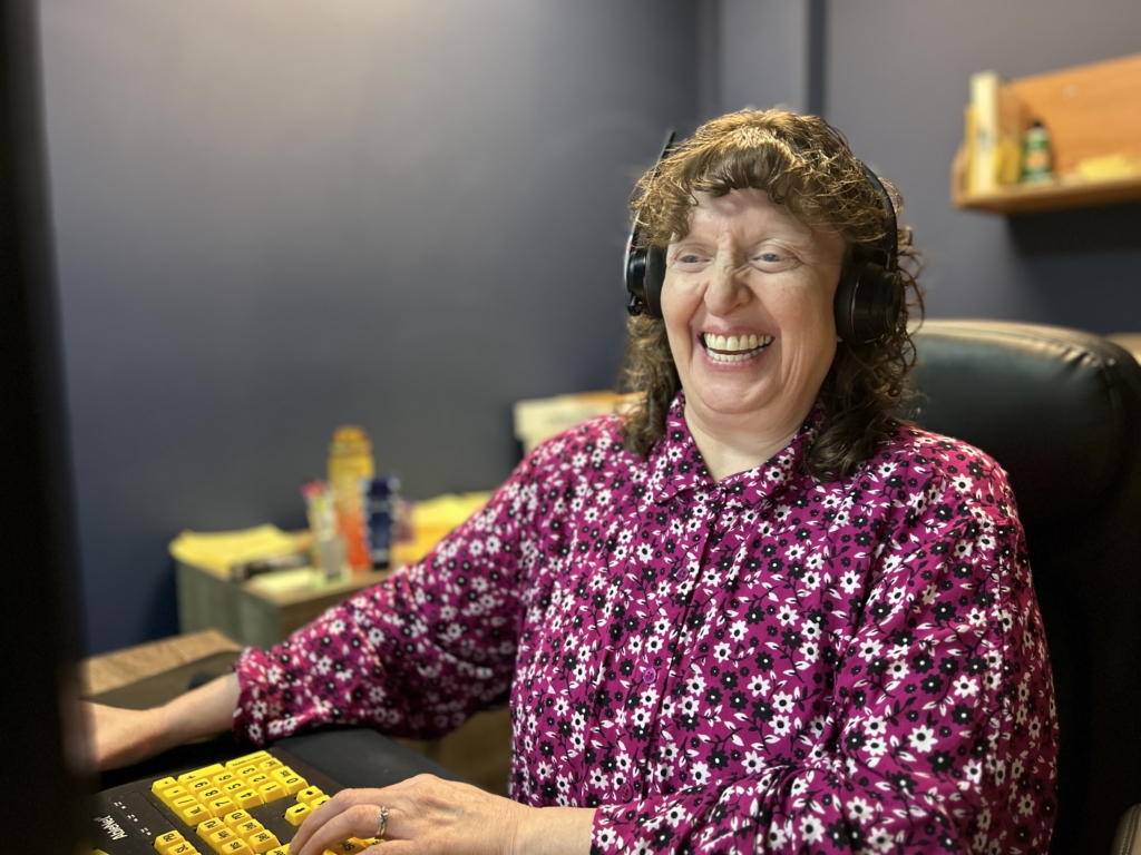 Melinda Slovernick at her workstation, with her hands on the keyboard, smiling.