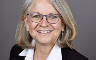 Portrait of a white woman with straight shoulder length gray blonde hair, smiling.