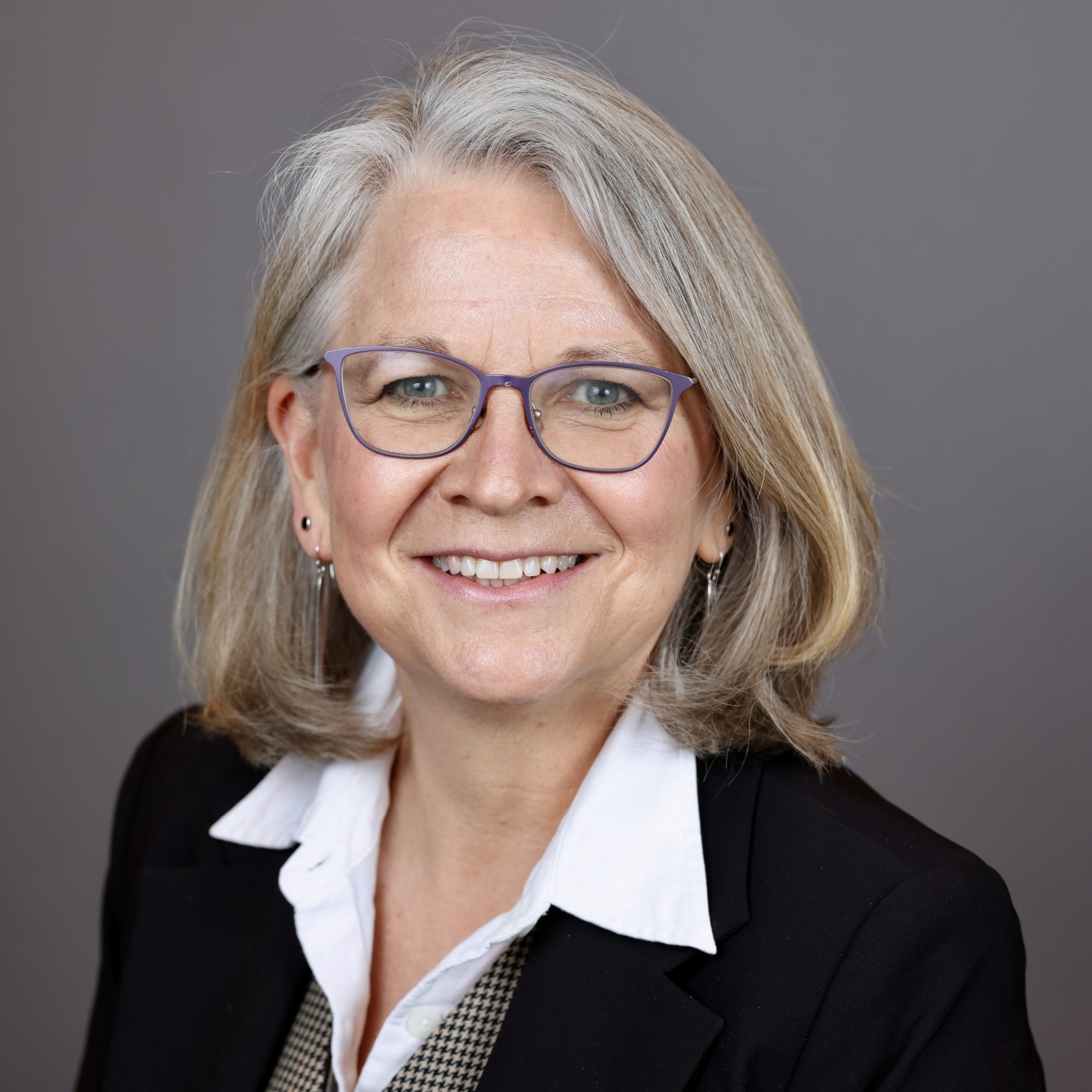 Portrait of a white woman with straight shoulder length gray blonde hair, smiling.