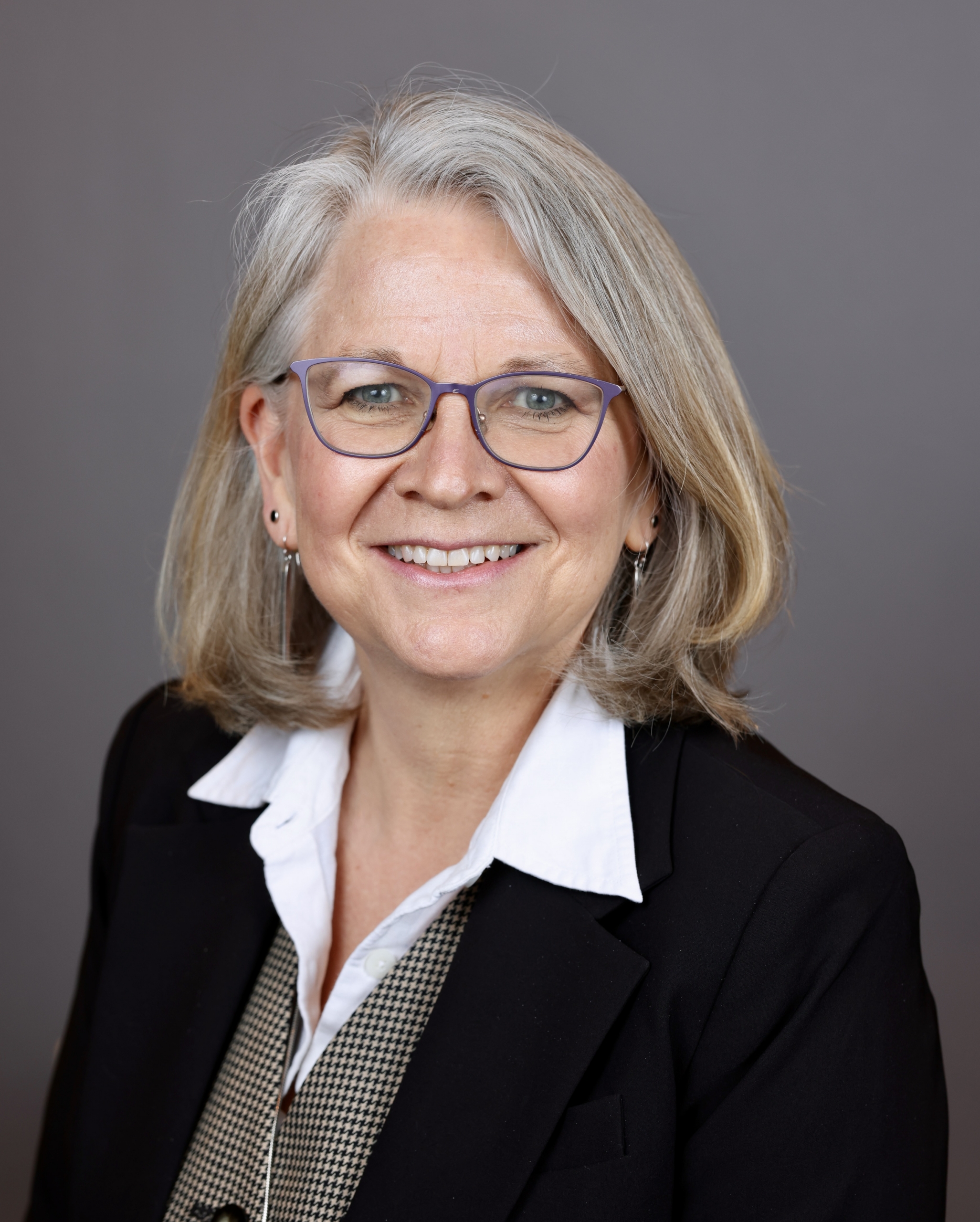 Portrait of a white woman with straight shoulder length gray blonde hair, smiling.