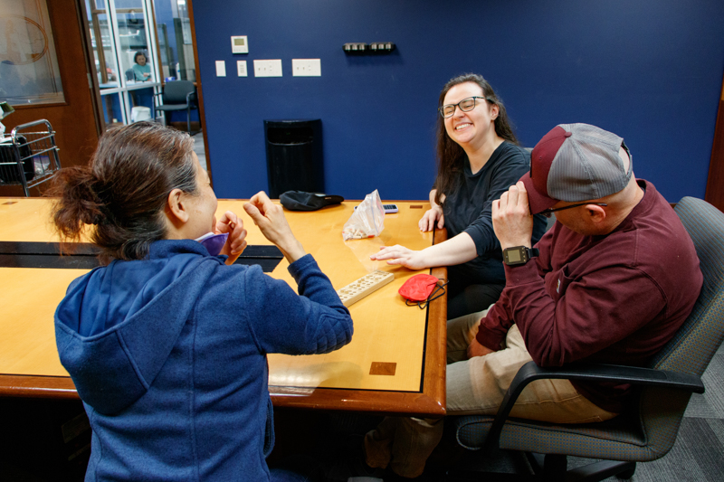 A group of people who are DeafBlind sit in a meeting room and smile while communicating in ASL