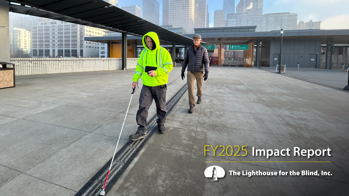 A DeafBlind man wearing a high-vis jacket uses a miniguide and a white cane in Downtown Seattle while an Orientation and Mobility Instructor follows behind