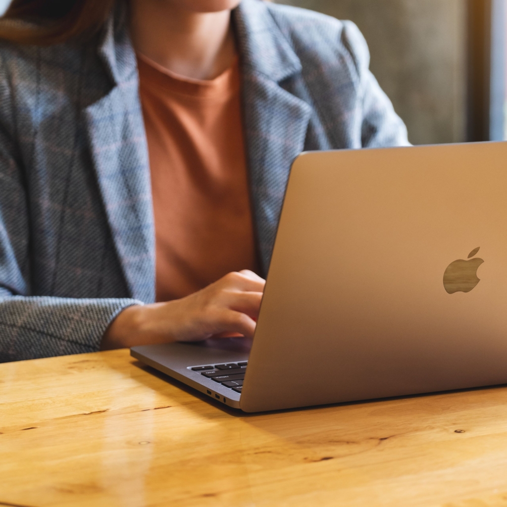 Cropped Image of a woman in a blazer using a Mac computer; you do not see her head, just the top of her torso.